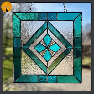 May include: A square stained glass panel with a geometric design. The panel features a central diamond shape with a turquoise starburst, surrounded by teal and clear textured glass. The panel is framed in black and hangs from a chain.