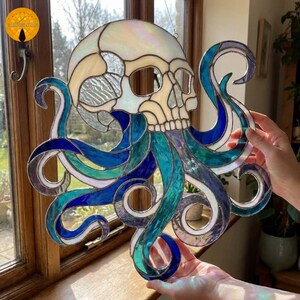 May include: A stained glass suncatcher featuring a human skull at the top with multiple flowing octopus tentacles extending downwards. The piece is constructed with iridescent white, deep blue, and teal glass segments joined by dark metal solder lines.
