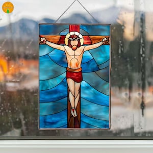 Puede incluir: Panel de vidrieras que representa a Jesús en la cruz. La obra presenta una cruz marrón, una figura con un taparrabos rojo y un halo. El fondo es un mosaico de vidrio azul y turquesa, con una cadena para colgar.