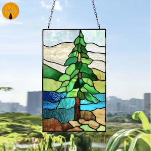 May include: Stained glass panel featuring a stylized evergreen tree in shades of green, brown, and blue. The panel is rectangular and hangs from a chain. The background shows a landscape with mountains and water.