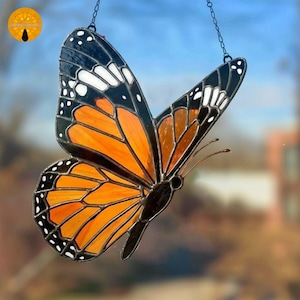 Puede incluir: Atrapasoles de mariposa de vidrieras con alas naranjas, negras y blancas. La mariposa está suspendida por una cadena. Las alas tienen un patrón detallado y el cuerpo es negro. Diseñado para capturar la luz.