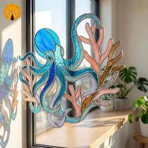 Può includere: Un acchiappasole in vetro colorato raffigurante un polpo blu con tentacoli in vetro testurizzato intrecciati a rami di corallo rosa chiaro e ambra. L'oggetto è composto da più segmenti di vetro uniti da linee di saldatura in metallo scuro.