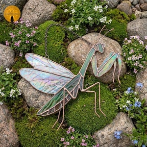 Puede incluir: Un atrapasoles de vidrieras con forma de mantis religiosa, con alas iridiscentes y un cuerpo verde construido con líneas de soldadura de cobre. La figura del insecto incluye dos largas antenas y está suspendida por una fina cadena de metal.