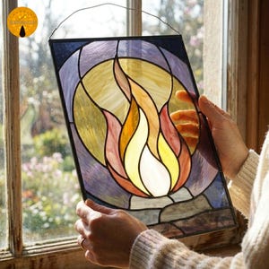 Peut inclure: Panneau de vitrail représentant une flamme. L'œuvre d'art présente une palette de couleurs vives de jaune, orange, rouge et violet. Le verre est encadré en noir et est suspendu par un fil.