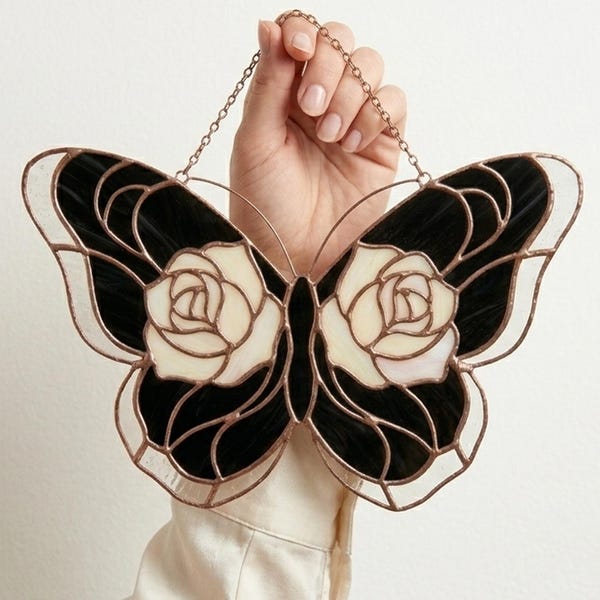 Puede incluir: Una mariposa de vidriera con alas negras y blancas, con diseños de rosas. La mariposa se sujeta con una cadena de cobre y tiene un borde color cobre. Una pieza decorativa para la decoración del hogar.