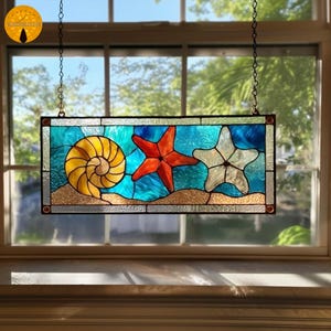 May include: Stained glass window panel featuring a seashell and two starfish against a blue and tan background. The panel is rectangular and hangs from chains. The window is in front of a window with a view of trees.