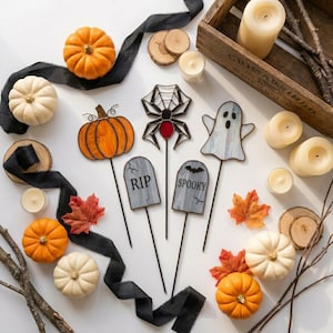 May include: A collection of five stained glass Halloween decorations on metal stakes, including an orange pumpkin, a black and red spider, a white ghost, and two gray tombstones labeled RIP and SPOOKY, surrounded by small pumpkins and candles.