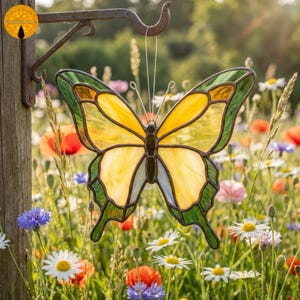 May include: A stained glass butterfly with yellow and green wings hangs from a metal hook. The butterfly's wings are a mosaic of yellow, green, and amber glass. The background is a field of wildflowers.