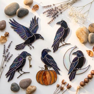 May include: Five stained glass raven ornaments featuring dark purple and black glass with metal solder lines. One raven is in flight, one perches on a branch with a key, one sits on a pumpkin, one perches on a branch, and one sits on a crescent moon.