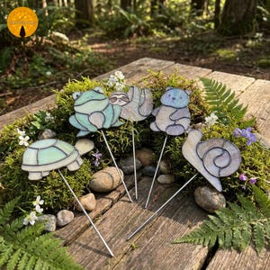 May include: A collection of whimsical stained glass garden stakes featuring a turtle, frog, sloth, bear, and snail. Each animal is crafted with pastel-colored glass and mounted on a metal stake, perfect for adding a touch of nature-inspired art to any garden or outdoor space.