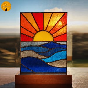 May include: A stained glass panel depicting a sunset over the ocean. The sun is a bright yellow, with orange and red rays. The ocean is represented by blue and gray waves. The panel is set on a wooden base.