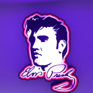 Può includere: Un'insegna al neon viola e bianca raffigurante un profilo di Elvis Presley con la sua firma. L'insegna ha un contorno rosso e un cavo di alimentazione nero. Lo sfondo è viola pieno.