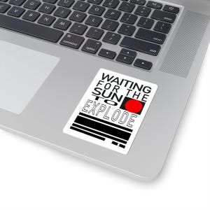Puede incluir: Una pegatina blanca con texto negro que dice "WAITING FOR THE SUN TO EXPLODE". Un círculo rojo está al lado de la palabra "SUN".