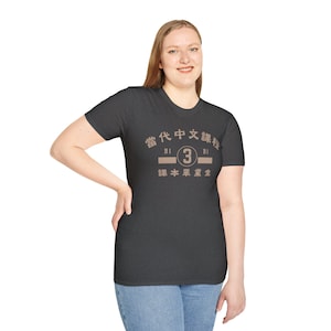 May include: Dark gray t-shirt with a crew neck. The shirt features a beige graphic with Chinese characters and the number 3. The text on the shirt reads "Contemporary Chinese Course" and "Textbook Graduates".