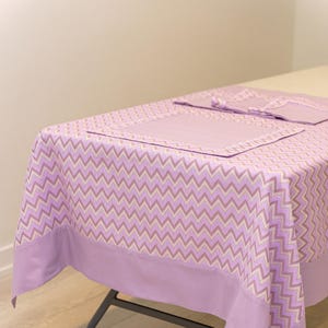 May include: A purple tablecloth with a chevron pattern and a solid purple border. The tablecloth is set with a matching placemat and napkins.