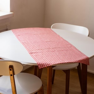 Puede incluir: Una mesa redonda blanca con un camino de mesa a cuadros rojo y blanco. La mesa tiene cuatro sillas blancas.