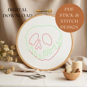 Puede incluir: Un bastidor de bordado de madera con tela blanca muestra un contorno rojo y verde de un dise&ntilde;o de calavera. El texto "DIGITAL DOWNLOAD" est&aacute; a la izquierda y "PDF STICK & STITCH DESIGN" a la derecha, en un c&iacute;rculo marr&oacute;n.