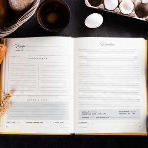 May include: An open recipe book with yellow edges, surrounded by baking ingredients. A loaf of bread, eggs, flour, and milk are arranged around the book. The book has sections for ingredients, directions, and notes.