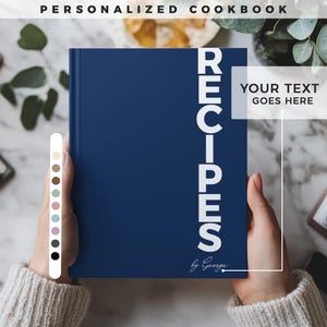 Könnte beinhalten: Ein marineblaues Kochbuch mit dem Wort "RECIPES" in weißem, vertikalem Text. Der Text "Your text goes here" ist ebenfalls sichtbar. Das Kochbuch wird von einer Person gehalten, die einen cremefarbenen Pullover trägt. Die Worte "Personalized Cookbook" stehen oben.