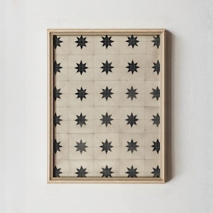 May include: A framed print with a repeating pattern of black eight-pointed stars on a cream background. The stars are arranged in a grid, and the frame is a light beige. This artwork would be suitable for home decor.