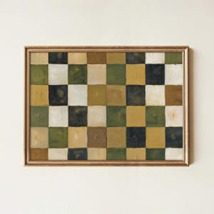 May include: A framed artwork featuring a checkerboard pattern in various muted colors. The squares are painted in shades of green, brown, black, white, and yellow. The artwork is encased in a gold-colored frame.