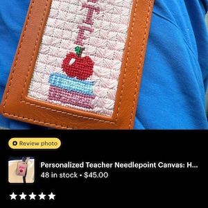 K&ouml;nnte beinhalten: Ein personalisierter Lehrer-Nadelspitzen-Leinwand-Gep&auml;ckanh&auml;nger. Der Anh&auml;nger zeigt ein gesticktes Design eines Apfels, B&uuml;cher und das Wort "Teacher" in Rosa. Der Anh&auml;nger ist in braunem Leder eingefasst.