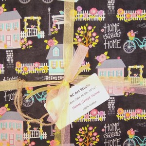 Könnte beinhalten: Ein Stoffbündel mit schwarzem Hintergrund, das ein sich wiederholendes Muster aus Häusern, Fahrrädern und floralen Elementen zeigt. Die Worte "Home Sweet Home" sind sichtbar. Das Bündel ist mit einem Band und einem Etikett "BC Art Studio" gebunden.