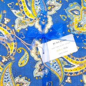 Könnte beinhalten: Blauer Stoff mit gelbem und weißem Paisley-Muster, gebunden mit blauem Band. Ein Etikett lautet: "BC Art Studio Layer Cake 35 Stk. 25.4cm x 25.4cm SUN & SEA 100% Cotton."