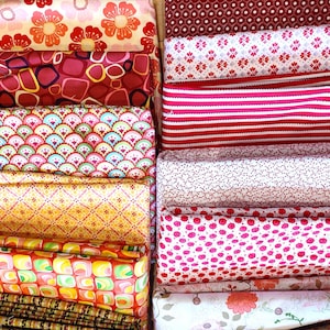 Könnte beinhalten: Eine Sammlung gefalteter Stoffe mit verschiedenen Mustern. Die Stoffe weisen florale, geometrische und gestreifte Designs in Rot-, Rosa-, Gelb- und Blautönen auf. Einige Stoffe haben kleine Tupfen, andere größere Blumendrucke.