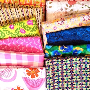 Könnte beinhalten: Eine Sammlung farbenfroher Stoffrollen mit verschiedenen Mustern. Designs umfassen florale, geometrische und gestreifte Muster in Rosa-, Grün-, Blau-, Gelb- und Orangetönen. Die Stoffe sind ordentlich gestapelt und zeigen eine Vielzahl von Texturen und Stilen.