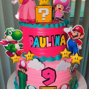 May include: A three-tiered pink birthday cake decorated with Super Mario characters, stars, and question mark blocks. The cake features the name "PAULINA" and the number "9". Decorations include Princess Peach, Mario, Yoshi, and Toad.