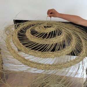 Puede incluir: Un gran sombrero redondo de paja tejido con un dise&ntilde;o en espiral. El sombrero est&aacute; hecho de materiales naturales y tiene un color marr&oacute;n claro.