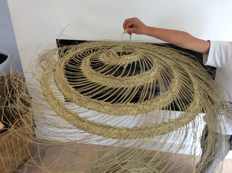 Puede incluir: Un gran sombrero redondo de paja tejido con un dise&ntilde;o en espiral. El sombrero est&aacute; hecho de materiales naturales y tiene un color marr&oacute;n claro.
