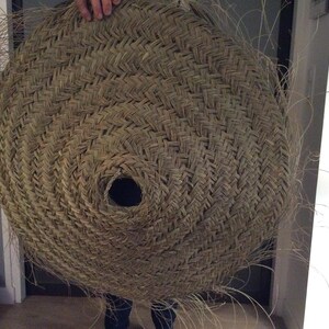 May include: A large, round, woven basket made of natural materials. The basket has a circular opening in the center and is made with a tight, intricate weave.