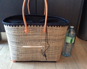 May include: A black and white woven tote bag with leather handles. The bag has a black fabric lining and a small zippered pocket on the front. A clear plastic water bottle is next to the bag.