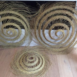 May include: Three woven wall decor pieces made of natural materials. The pieces are circular and feature a spiral design. The largest piece is approximately 24 inches in diameter.