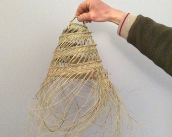 Puede incluir: Una pantalla de lámpara tejida de paja natural con un borde de flecos. La pantalla de la lámpara es de color marrón claro y tiene una forma cónica.