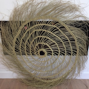 May include: A large, round, woven wall hanging with a spiral design. The hanging is made of natural fibers and has a fringe around the edge.