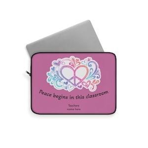 Può includere: Una custodia rosa per laptop con cerniera nera e un design a cuore con il simbolo della pace. Il design include un simbolo della pace a forma di cuore, cuori e il testo "Peace begins in this classroom".