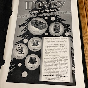 May include: A black and white advertisement for DeVry Moving Picture Cameras and Projectors. The ad features a Christmas tree with ornaments that are images of different DeVry cameras. The text in the ad reads "DeVry Moving Picture Cameras and Projectors" and "Put a DeVry Camera or Projector on your Christmas tree this year - it will be the outstanding gift of the season."