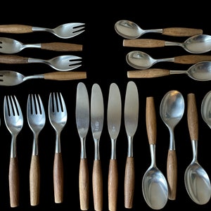 May include: A selection of vintage cutlery featuring stainless steel heads and wooden handles. The set includes forks, knives, and spoons, displayed against a black backdrop. The wooden handles exhibit a warm, natural wood grain.