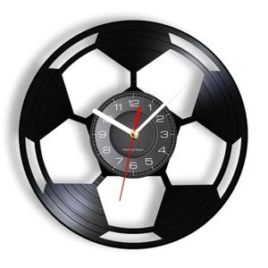 May include: A black vinyl record clock shaped like a soccer ball. The clock face is gray with black numbers and hands. The text "The Vinyl Clock" is printed on the clock face.
