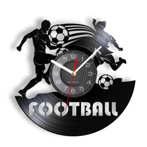 May include: Black vinyl record clock with a silhouette of two soccer players kicking a ball. The clock face is white with black numbers and hands. The words "FOOTBALL" are printed in silver below the clock face.