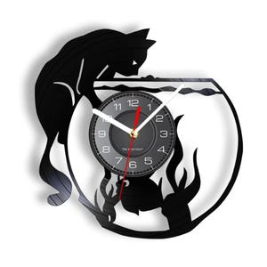Könnte beinhalten: Schwarze Schallplattenuhr mit einer Silhouette einer Katze, die in eine Fischschale mit einem Fisch darin schaut. Das Zifferblatt der Uhr ist schwarz mit weißen Zahlen und Zeigern.