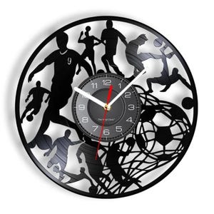 May include: Black vinyl record clock featuring a silhouette of soccer players in action. The clock face is black with white numbers and hands. The text "The Vinyl Clock" is printed on the clock face.