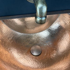 May include: A hammered copper sink with a round drain and a tap in the background.