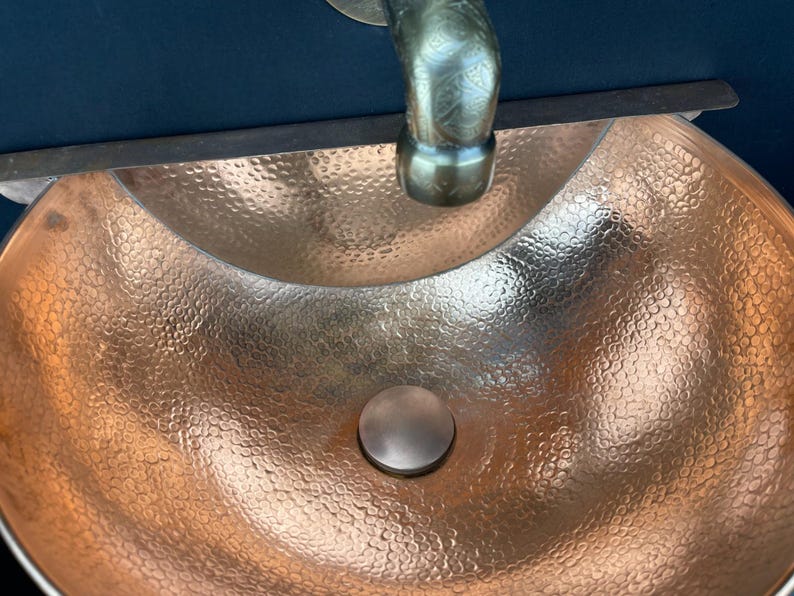 May include: A hammered copper sink with a round drain and a tap in the background.