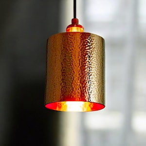 May include: A gold hammered metal pendant light with a red interior. The light is hanging from a wire.