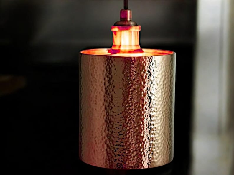 May include: A copper pendant light fixture with a hammered finish. The light is on and casting a warm glow.