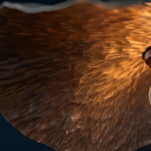May include: A close-up of a copper-toned lampshade with a textured surface. The lampshade is lit by a light bulb, casting a warm glow.